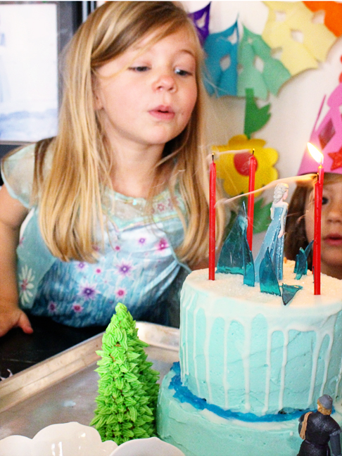 little girl blowing out candles on frozen cake