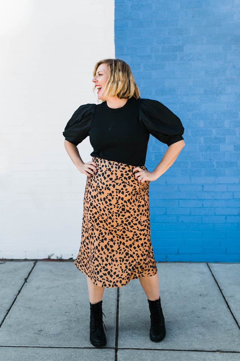 woman with hands on hips in black shirt and leopard print skirt with combat boots