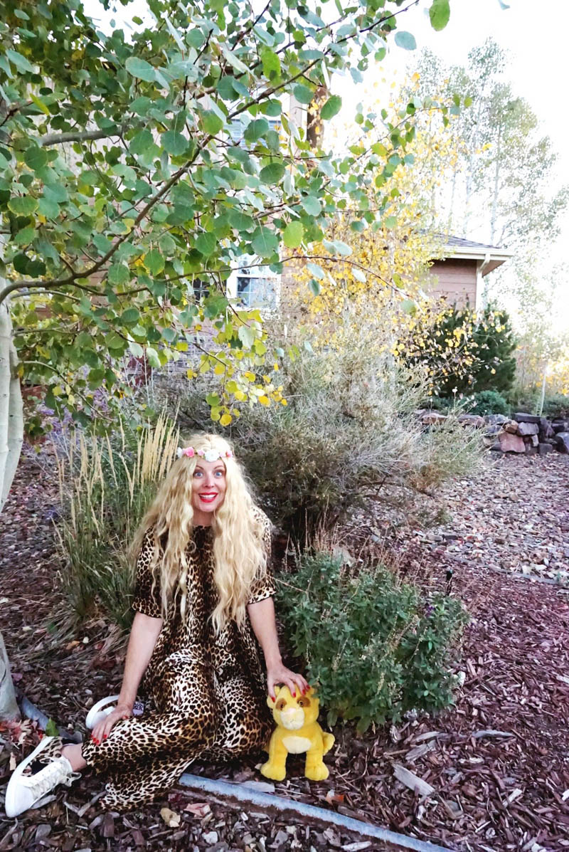 woman dressed as Carole Baskin sits by bushes with stuffed lion