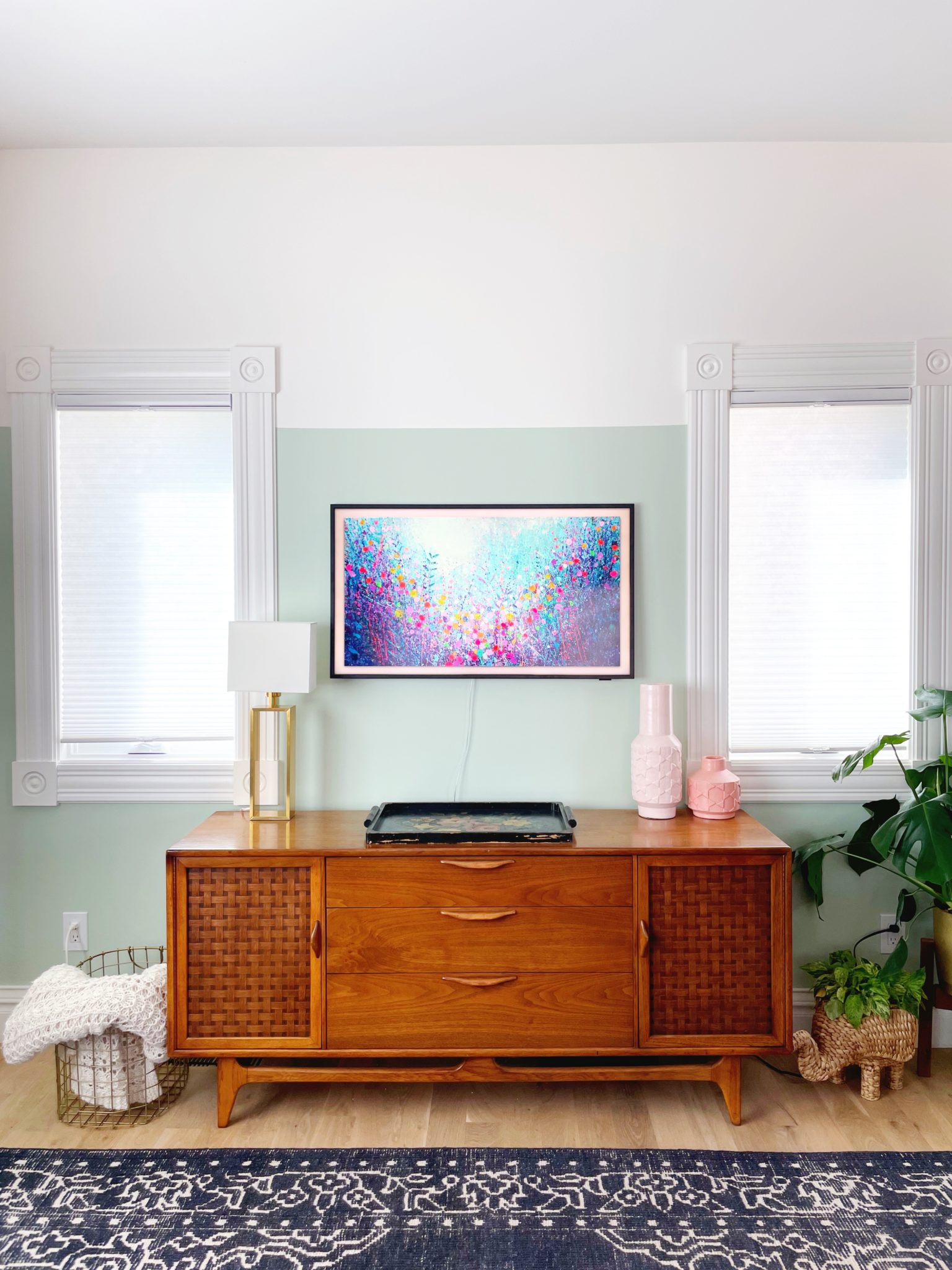 A TV on a wall with a sideboard and plants and decorative objects.